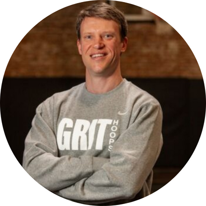 New York Grit Coach Brad Wetherell, posing in their gray and white sweatshirt, arms crossed and smiling confidently against a basketball court backdrop for their official coach photo.