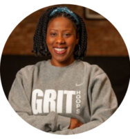 New York Grit Coach Camille Edwards, posing in their gray and white sweatshirt, arms crossed and smiling confidently against a basketball court backdrop for their official coach photo.